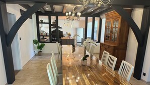 A spacious dining area with a large wooden table, white chairs, and a chandelier. - Huge estate with swimming pool, cinema, reception hall, boules pitch and more (Nérac)