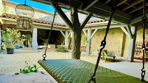 A rustic outdoor seating area with a swing set, a hanging lantern, and a building with a tiled roof in the background. - Huge estate with swimming pool, cinema, reception hall, boules pitch and more (Nérac)