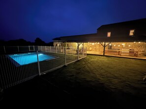 A swimming pool surrounded by a metal fence, a stone building with a covered patio area, and string lights. - Huge estate with swimming pool, cinema, reception hall, boules pitch and more (Nérac)