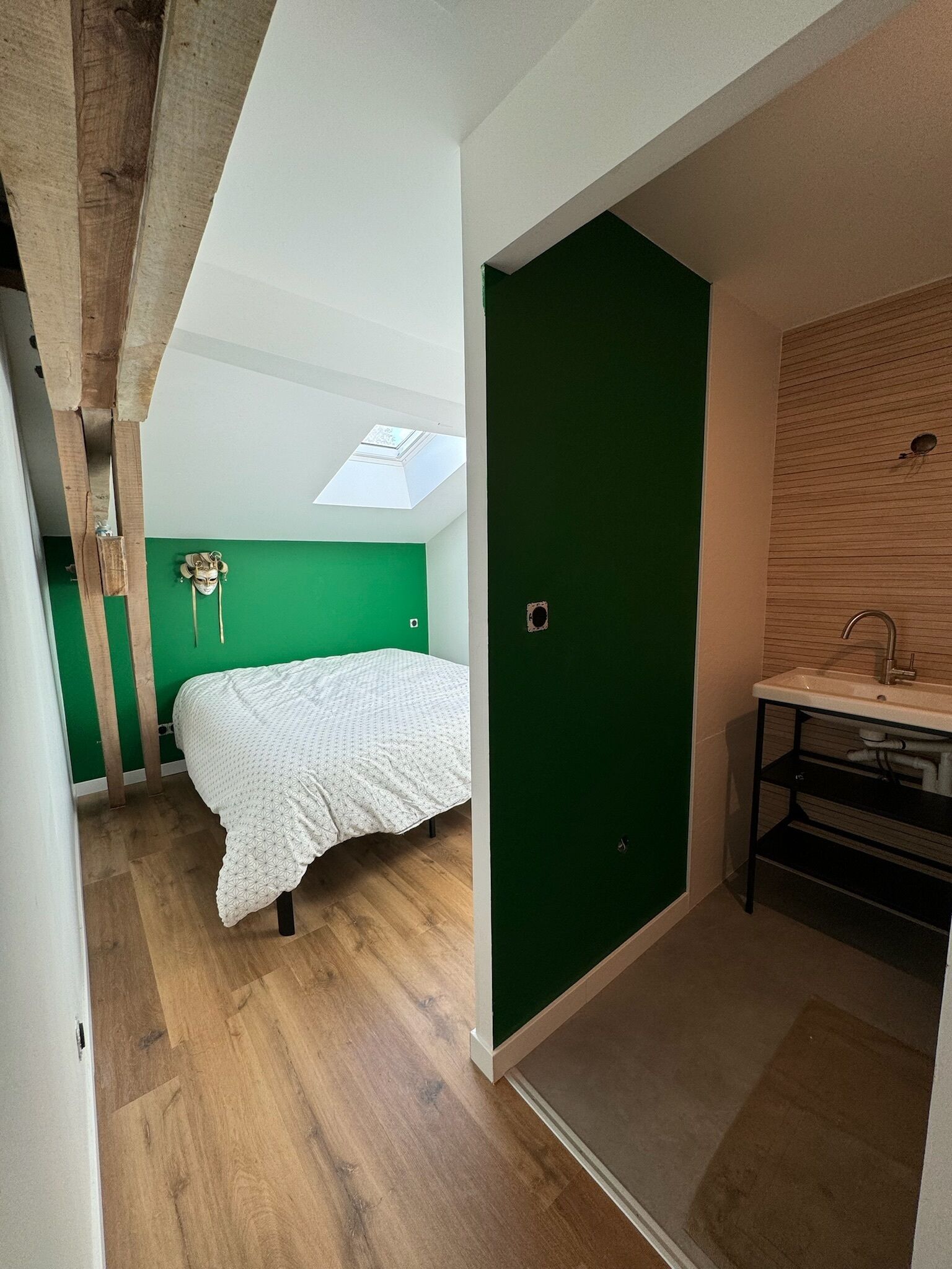 A bedroom with a bed, a green wall, a skylight, and a wooden ceiling.