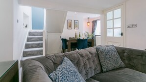 Ett vardagsrum med en grå soffa, mönstrade kuddar, en trappa och en matplats med ett bord och stolar.