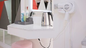 A bathroom vanity with a hairdryer, a kettle, and toiletries.