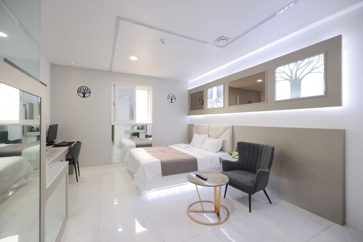 A modern hotel room with a bed, desk, chair, and a small round table.