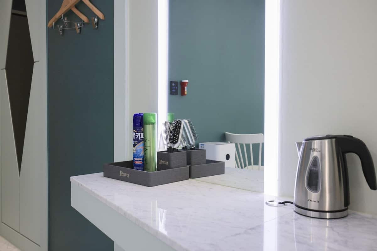 A kitchen counter with a kettle, a bottle of shampoo, and a brush.