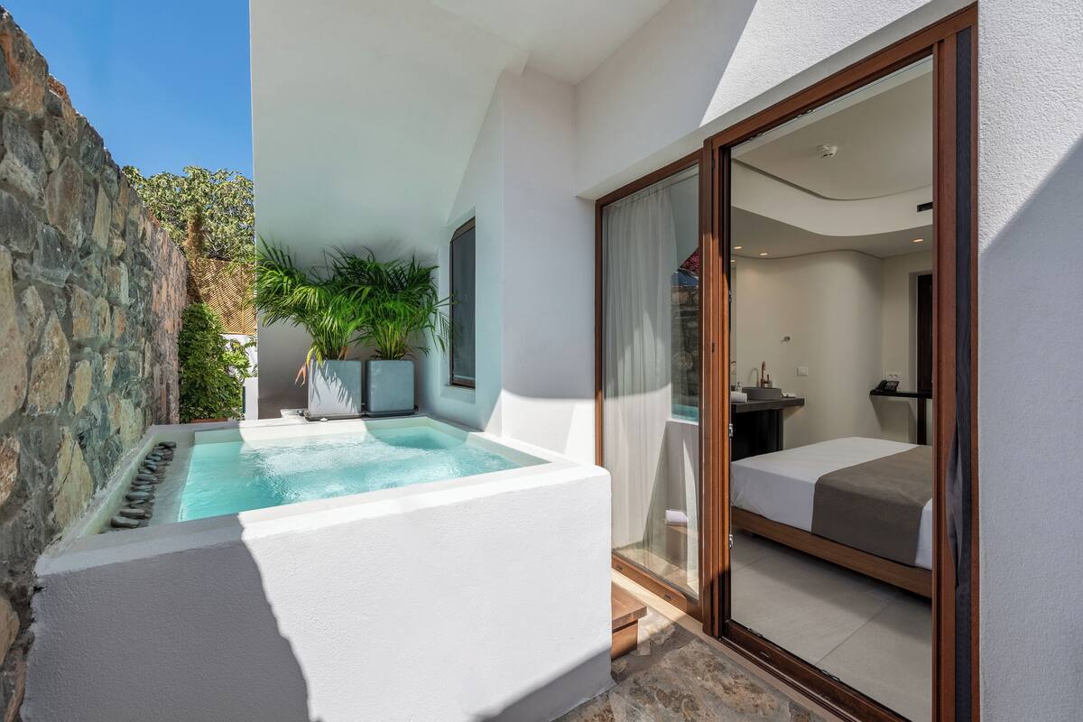 Ein modernes Hotelzimmer mit privatem Pool, einem Balkon mit Steinwand und einer großen Schiebeglasdoor, die zu einem Badezimmer führt.