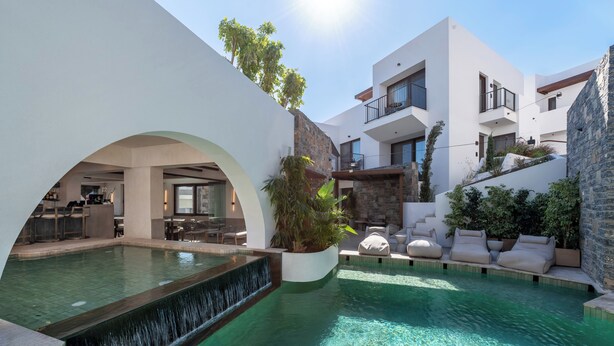 A modern pool area with a waterfall feature, outdoor seating, and a stone facade. - Elounda Stories Boutique Hotel (Agios Nikolaos)