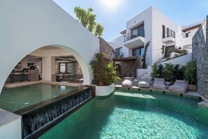 A modern pool area with a waterfall feature, outdoor seating, and a stone facade. - Elounda Stories Boutique Hotel (Agios Nikolaos)