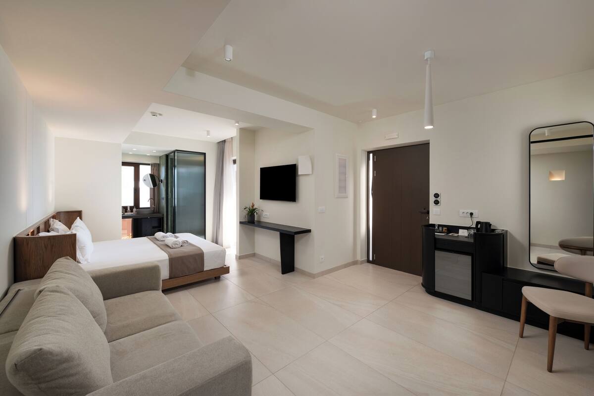Ein modernes Hotelzimmer mit Bett, Sofa, Schreibtisch, Spiegel und Fernseher.