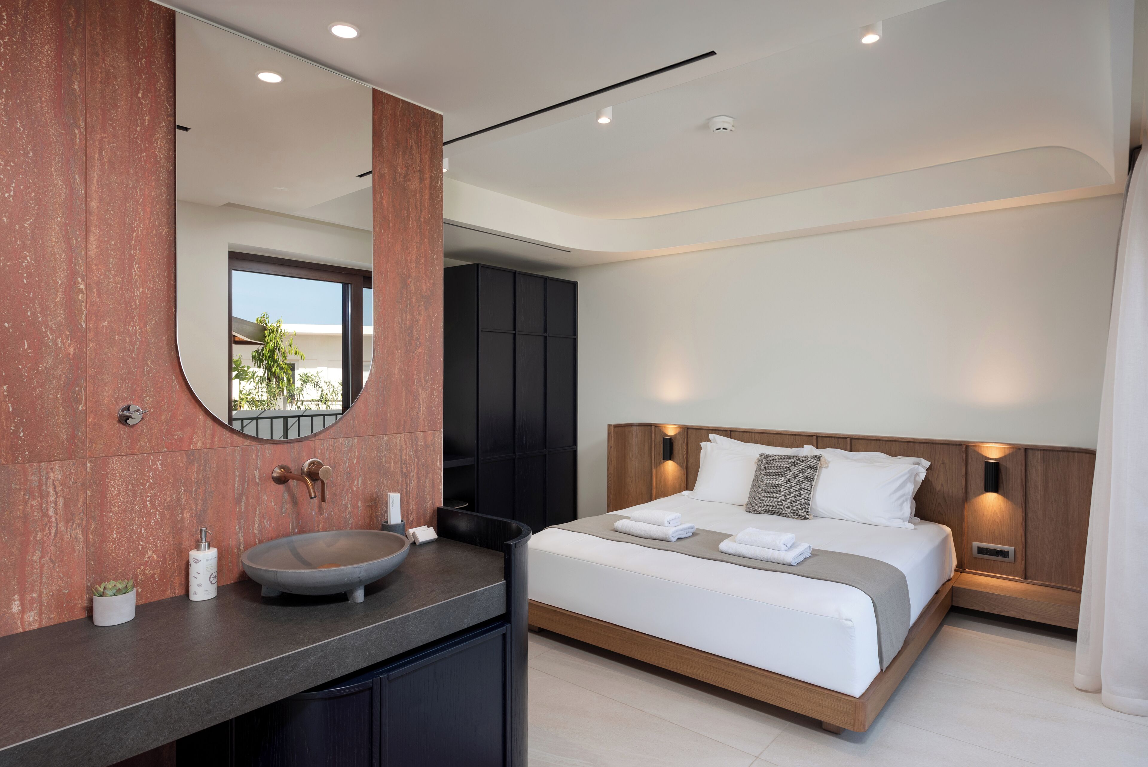 A modern hotel room with a large bed, a round sink, and a large mirror.