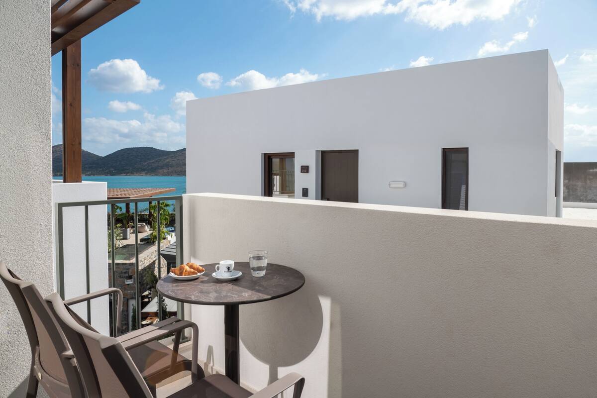 Ein Balkon mit Tisch, Stühlen und Blick auf das Meer und die Berge.