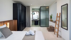 A modern hotel room with a bed, a wooden headboard, a bathroom with a sink and mirror, and a staircase leading to an upper level. - Elounda Stories Boutique Hotel (Agios Nikolaos)