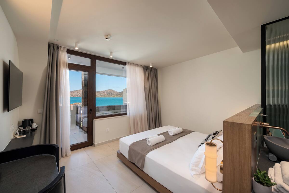 Ein modernes Hotelzimmer mit Bett, Schreibtisch, Stuhl, Bad und Meerblick.