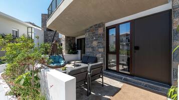 Un patio moderno al aire libre con un muro de piedra, una puerta corrediza de vidrio y una zona de estar con un banco acolchado y una mesita.