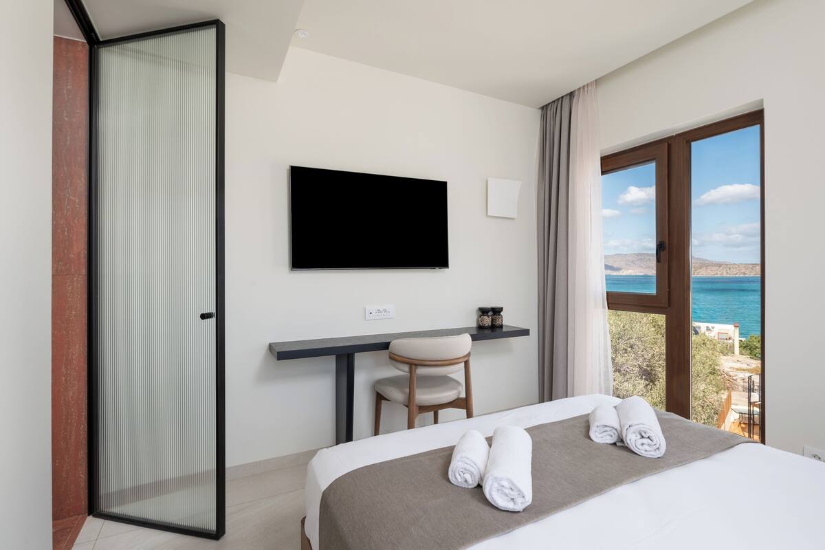 Ein Hotelzimmer mit Bett, Schreibtisch, Stuhl, Fernseher und Meerblick.