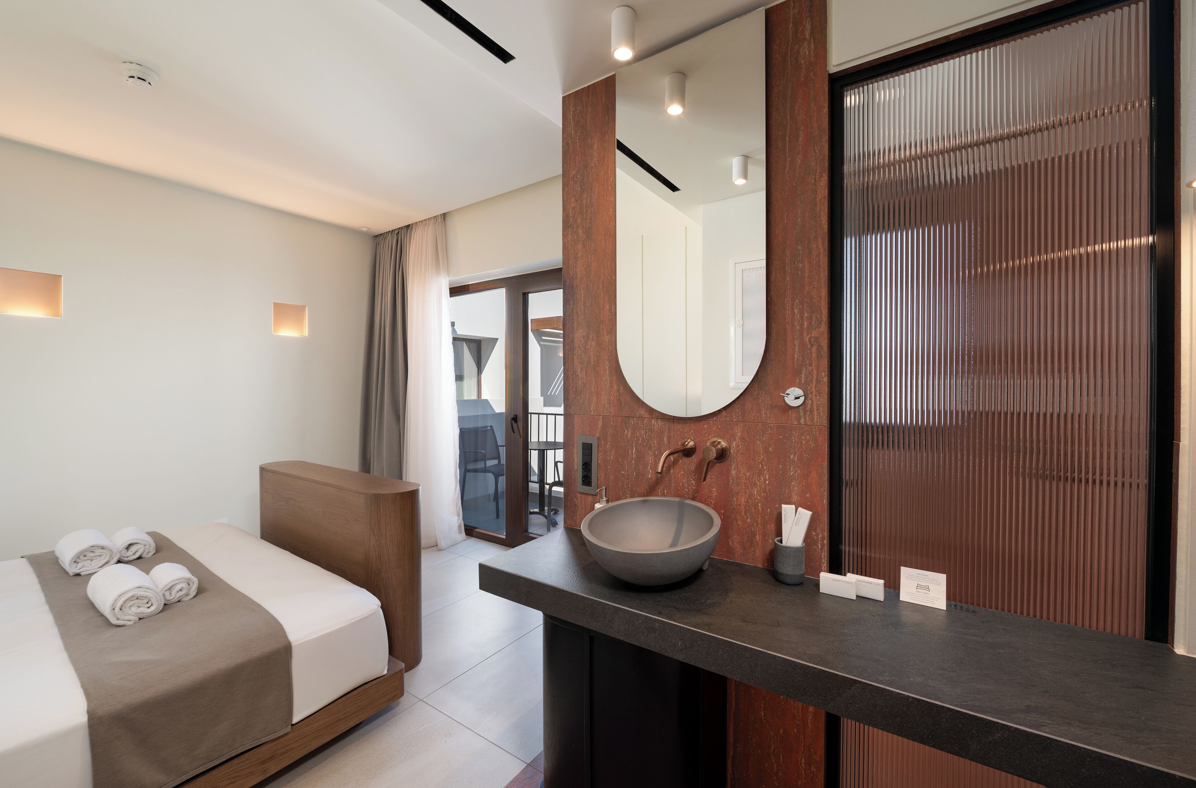 A modern hotel room with a bed, a large mirror, a round sink, and a wooden vanity.