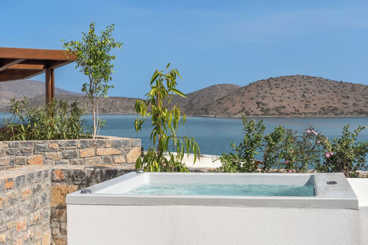 Ein Wellnessbereich mit Whirlpool, Steinwand und Blick auf das Meer und die Hügel.