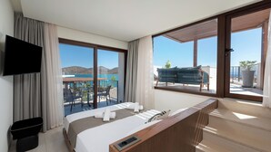 A modern hotel room with a large bed, a TV, and a balcony with a view of a pool and mountains. - Elounda Stories Boutique Hotel (Agios Nikolaos)