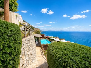 Una scala in pietra conduce a una zona piscina con vista sul mare.