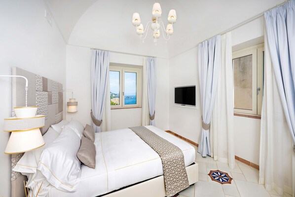 A bedroom with a bed, curtains, a TV, a chandelier, and a window with a view.
