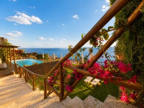A wooden staircase leading to a pool area with a view of the sea.