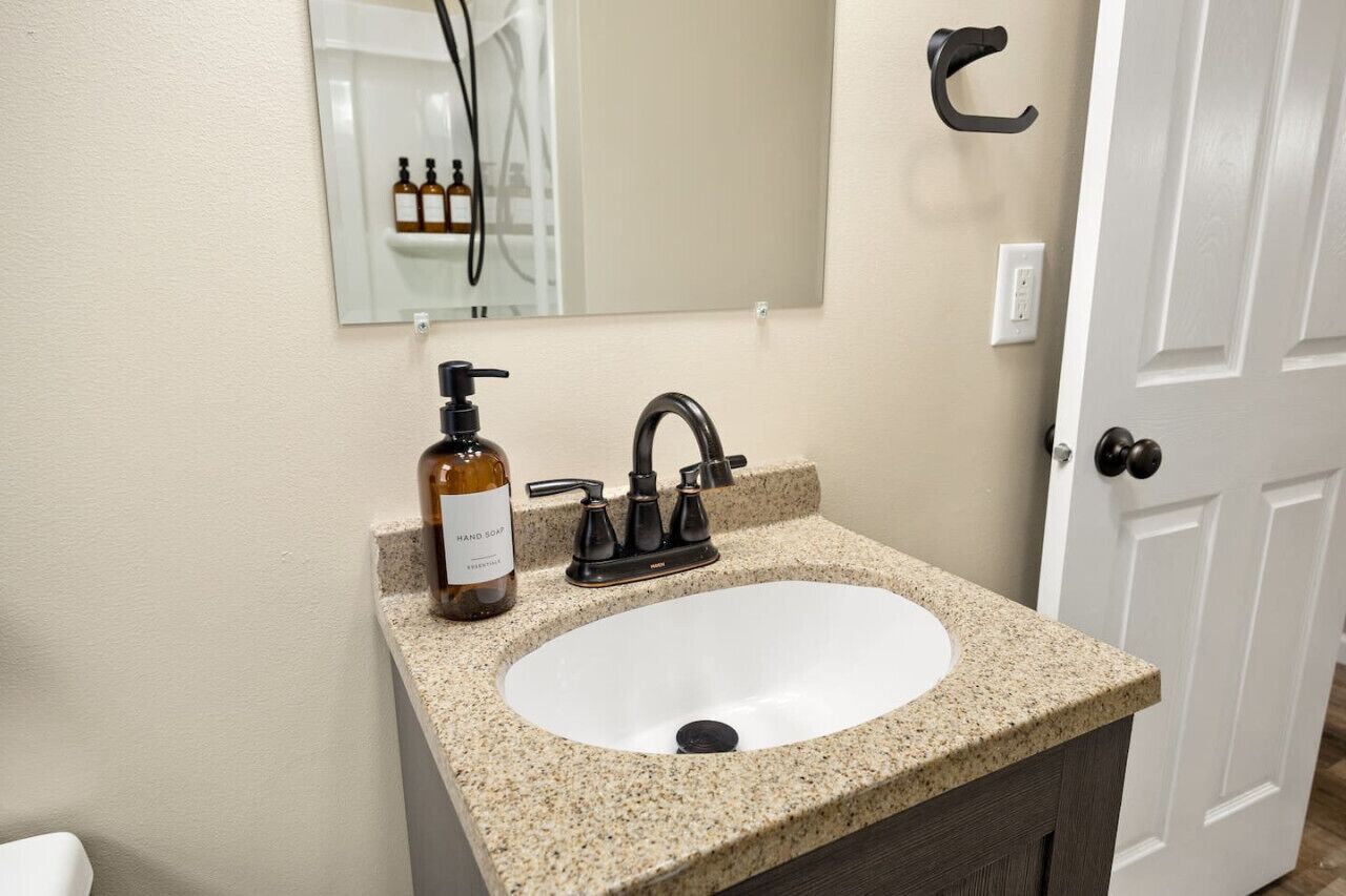 A bathroom with a granite countertop sink, a black faucet, a bottle of hand soap, and a mirror above the sink.