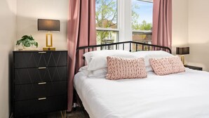 Een slaapkamer met een bed, twee nachtkastjes, een kaptafel en een raam met gordijnen.