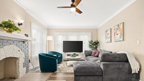 Een woonkamer met een open haard, een plafondventilator, een televisie en een bank.