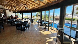 A restaurant with a pool view, wooden ceiling, and tiled floor.