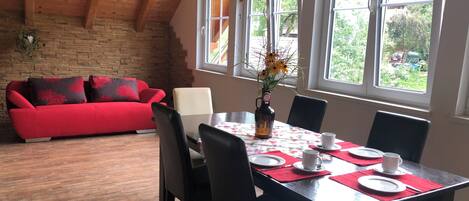 A dining area with a wooden table set for four, surrounded by chairs, and a red sofa in the background.
