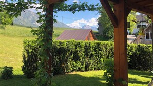 Une pergola en bois offrant une vue sur une maison et, au loin, sur des montagnes.