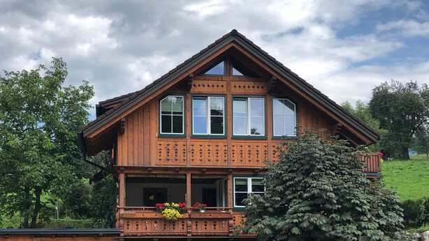 Un chalet en bois doté d’un balcon, de grandes fenêtres et d’un toit en pente.