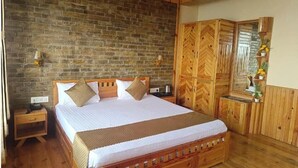 A wooden-framed bed with a brick wall behind it, a wooden wardrobe, and a mirror with a decorative plant. - Kasar Hill Top (Almora)
