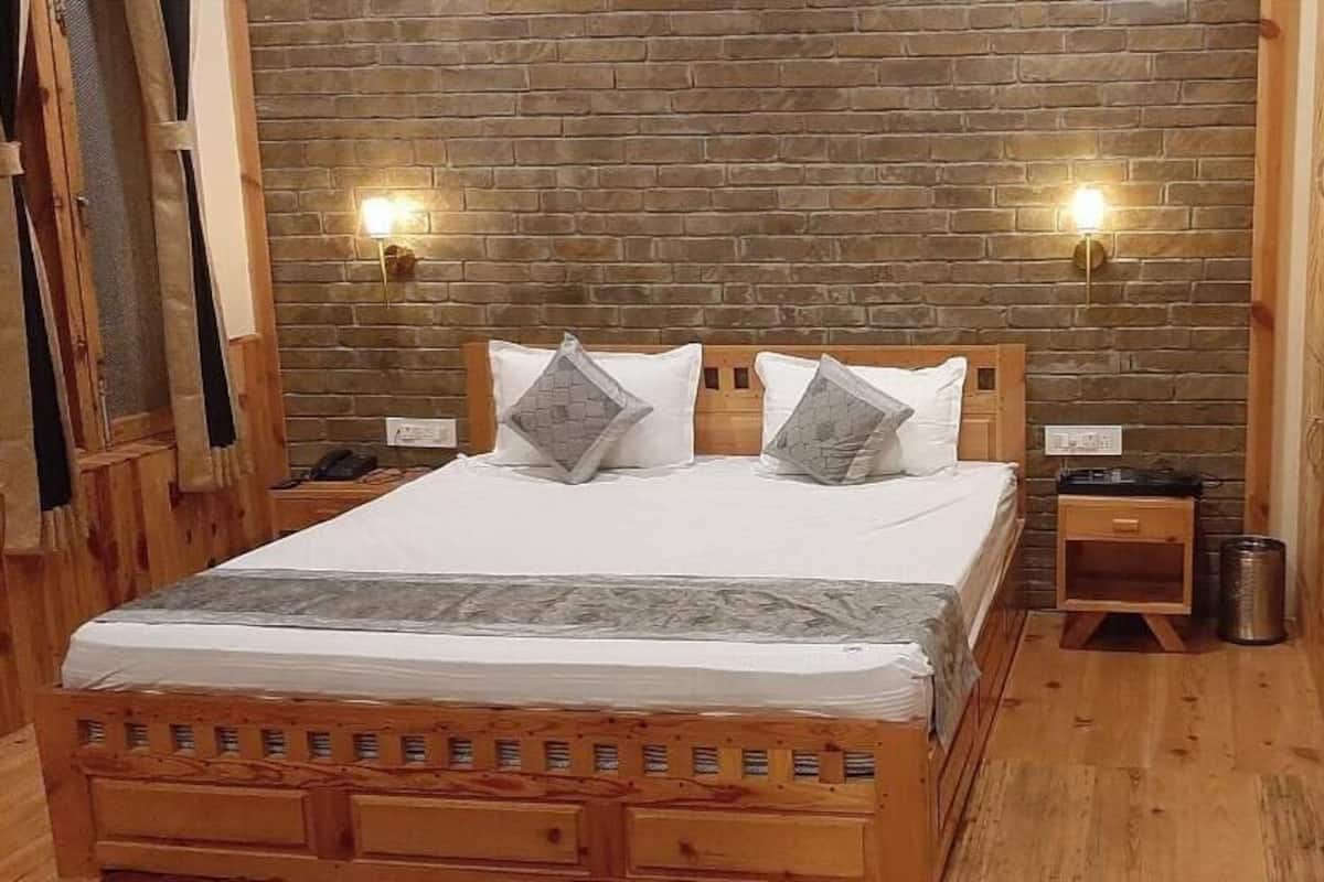 A wooden-framed bed with a white mattress and gray bedding, two wall-mounted lights, and a small wooden nightstand with a trash can.