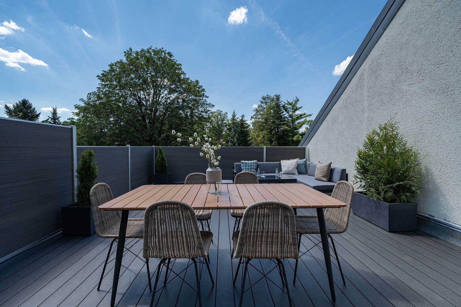 Una terraza de madera con una mesa de comedor y sillas, un sofá y una pequeña planta en maceta.