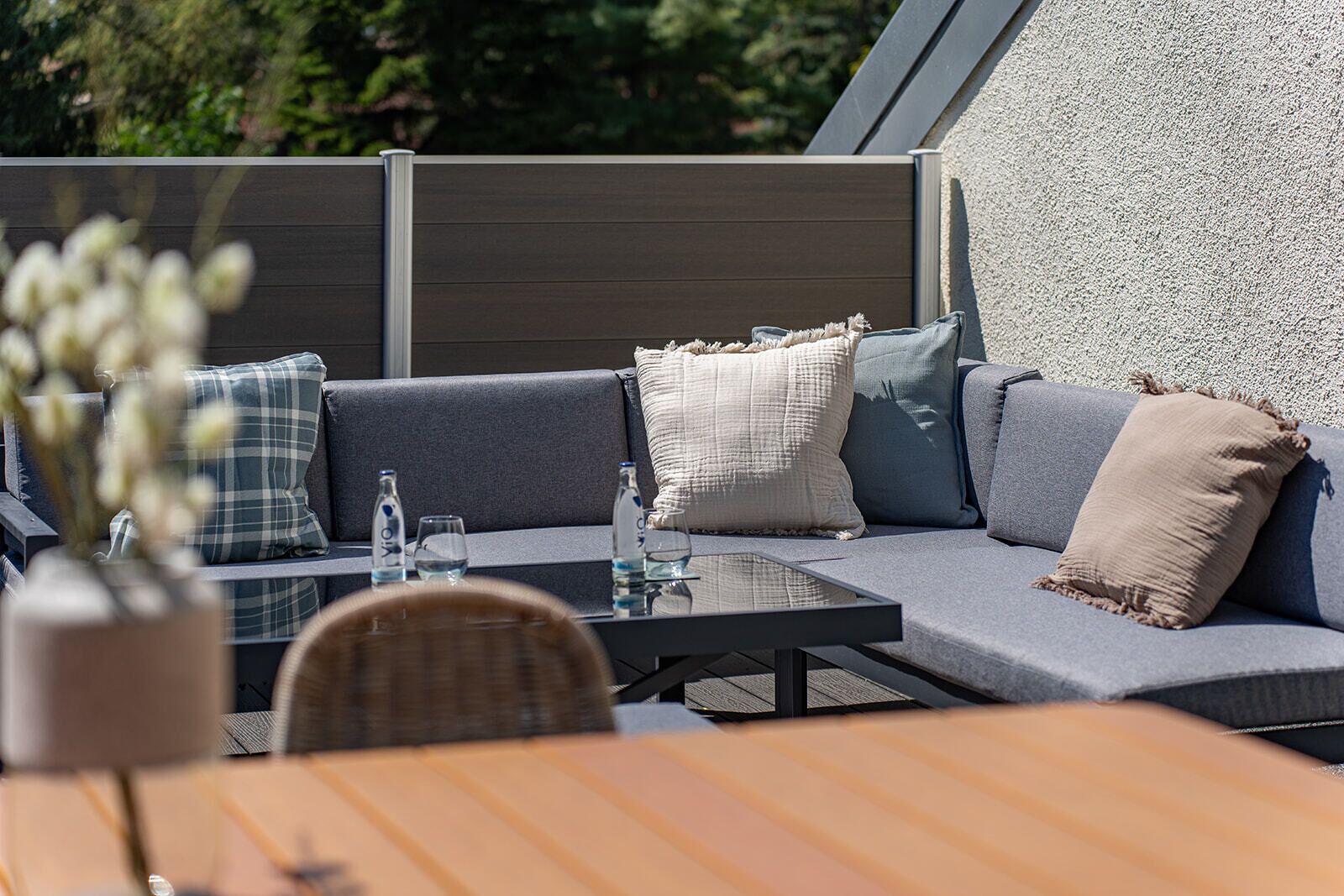 Et moderne udendørs opholdsområde med et glasbord, polstrede sofaer og mange puder.