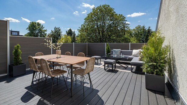 An outdoor patio with a wooden deck, a dining table with chairs, a sofa, and a small coffee table.