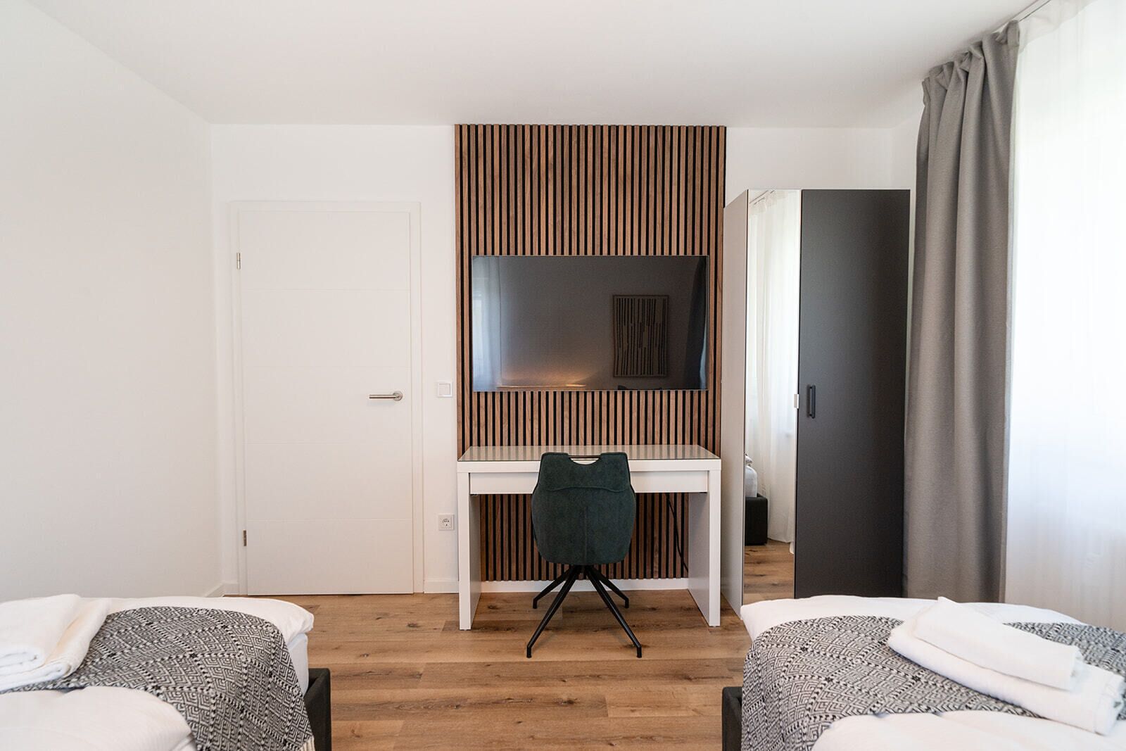 Ein Hotelzimmer mit weißem Schreibtisch, einem Sessel, einem Bett und einem Kleiderschrank.