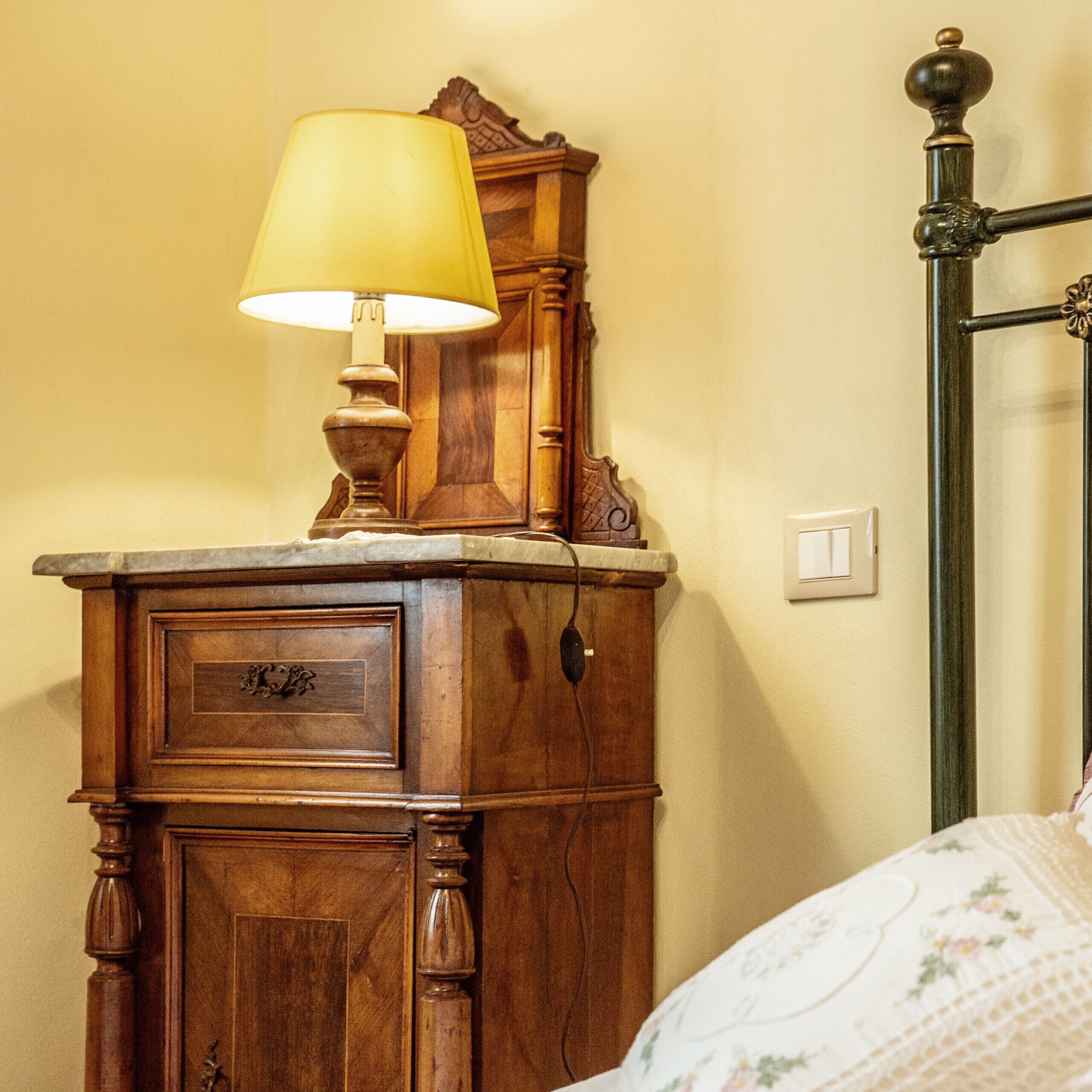 A wooden dresser with a lamp on top, a bed with floral bedding, and a metal bed frame.