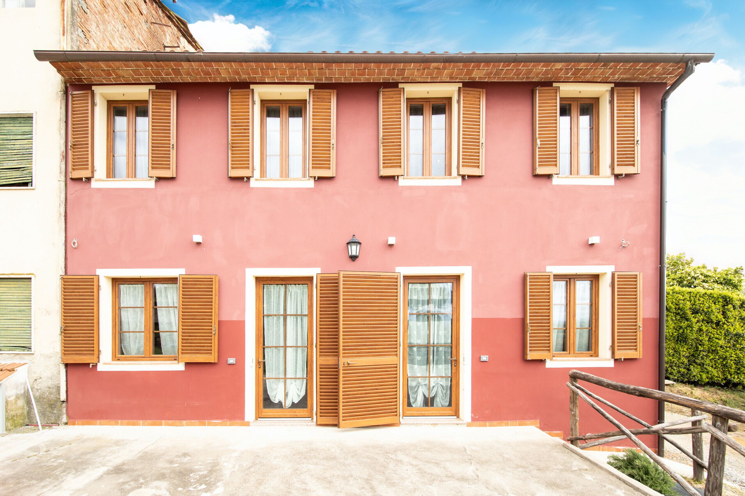 A two-story building with a red facade, wooden shutters on the windows, and a small balcony with a wooden railing.