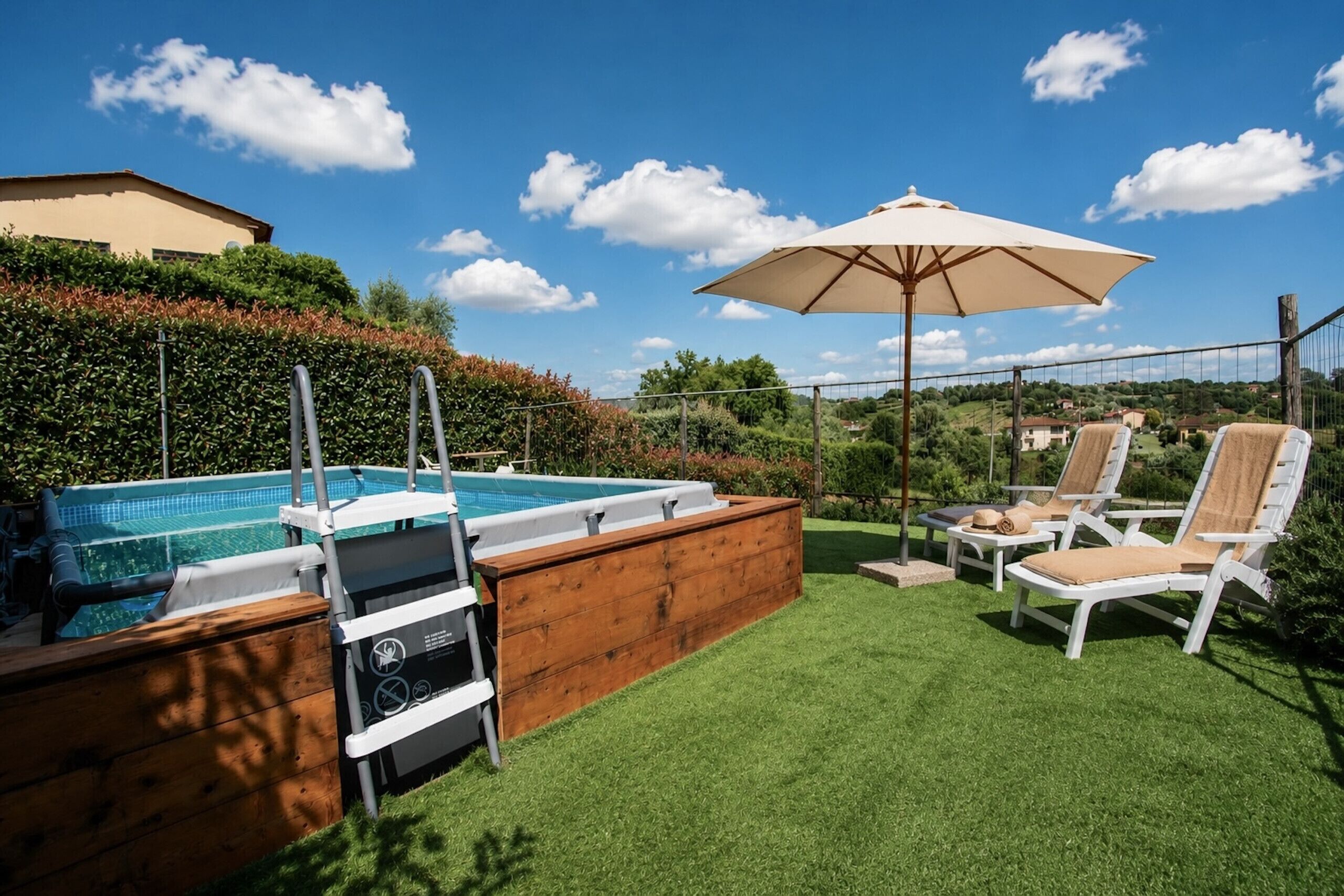 A backyard with a swimming pool, wooden deck, lounge chairs, and an umbrella.