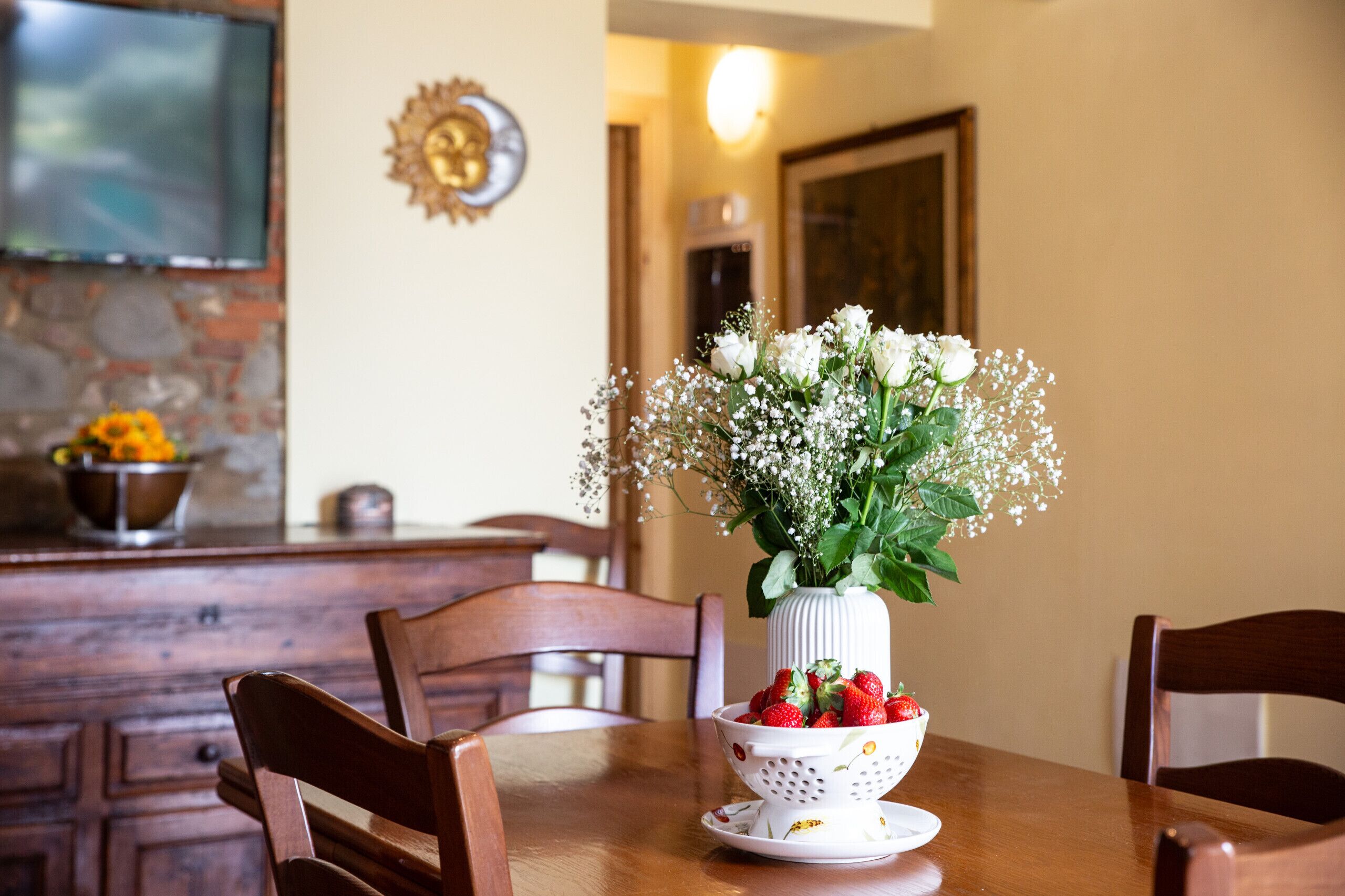 Un tavolo da pranzo con un vaso di fiori bianchi e una ciotola di fragole.