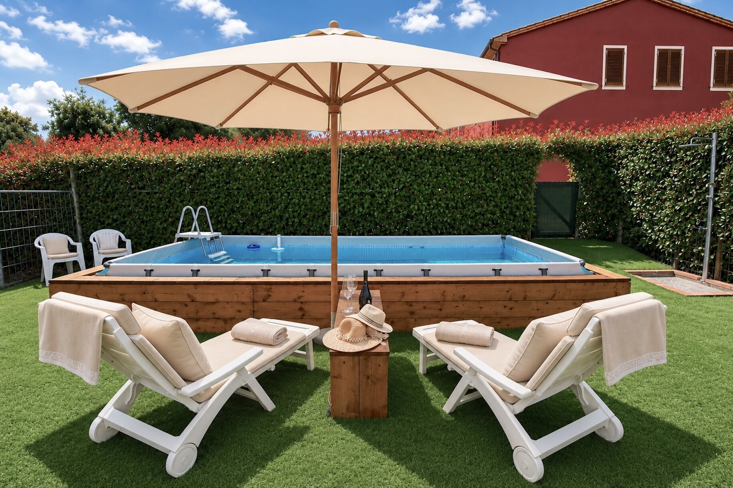 Une piscine rectangulaire avec une terrasse en bois, entourée de gazon synthétique, de deux chaises longues blanches et d’un grand parasol beige.