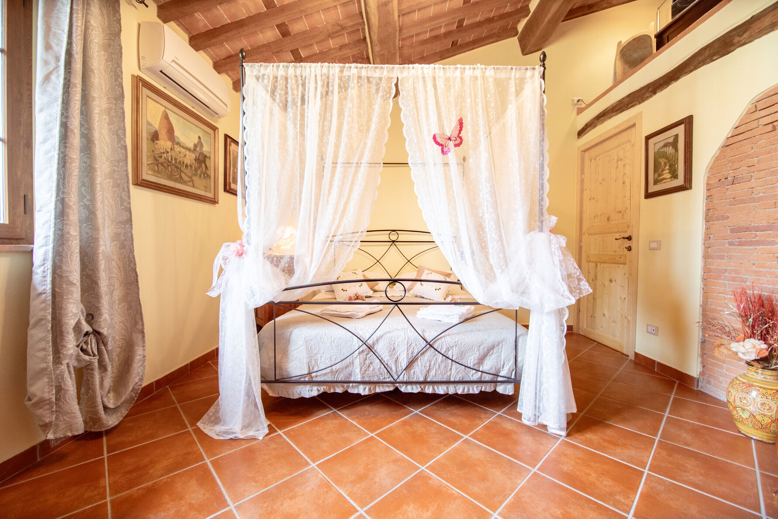 A bedroom with a four-poster bed, a wooden ceiling, and a tiled floor.