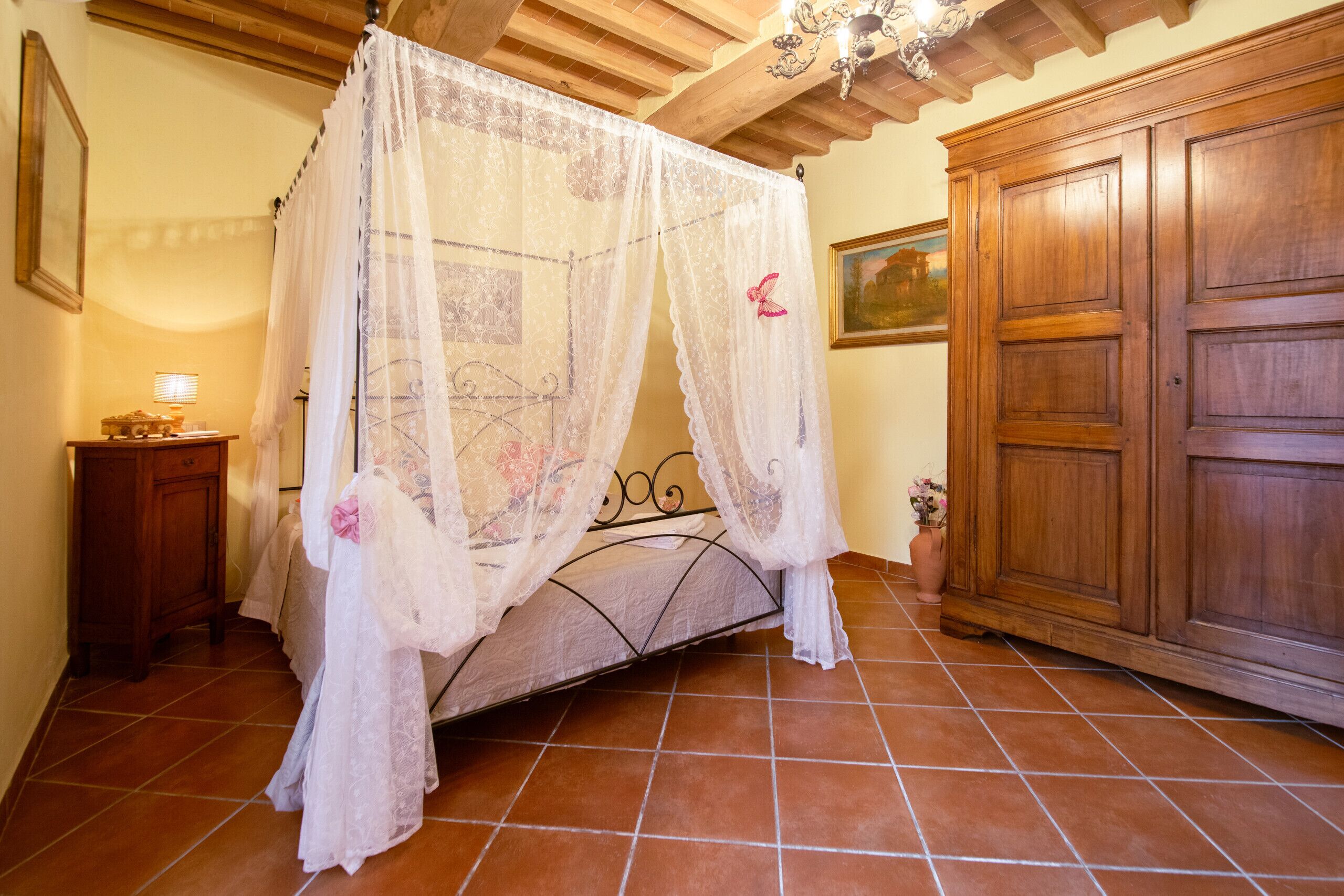 A bedroom with a four-poster bed, wooden wardrobe, and tiled floor.