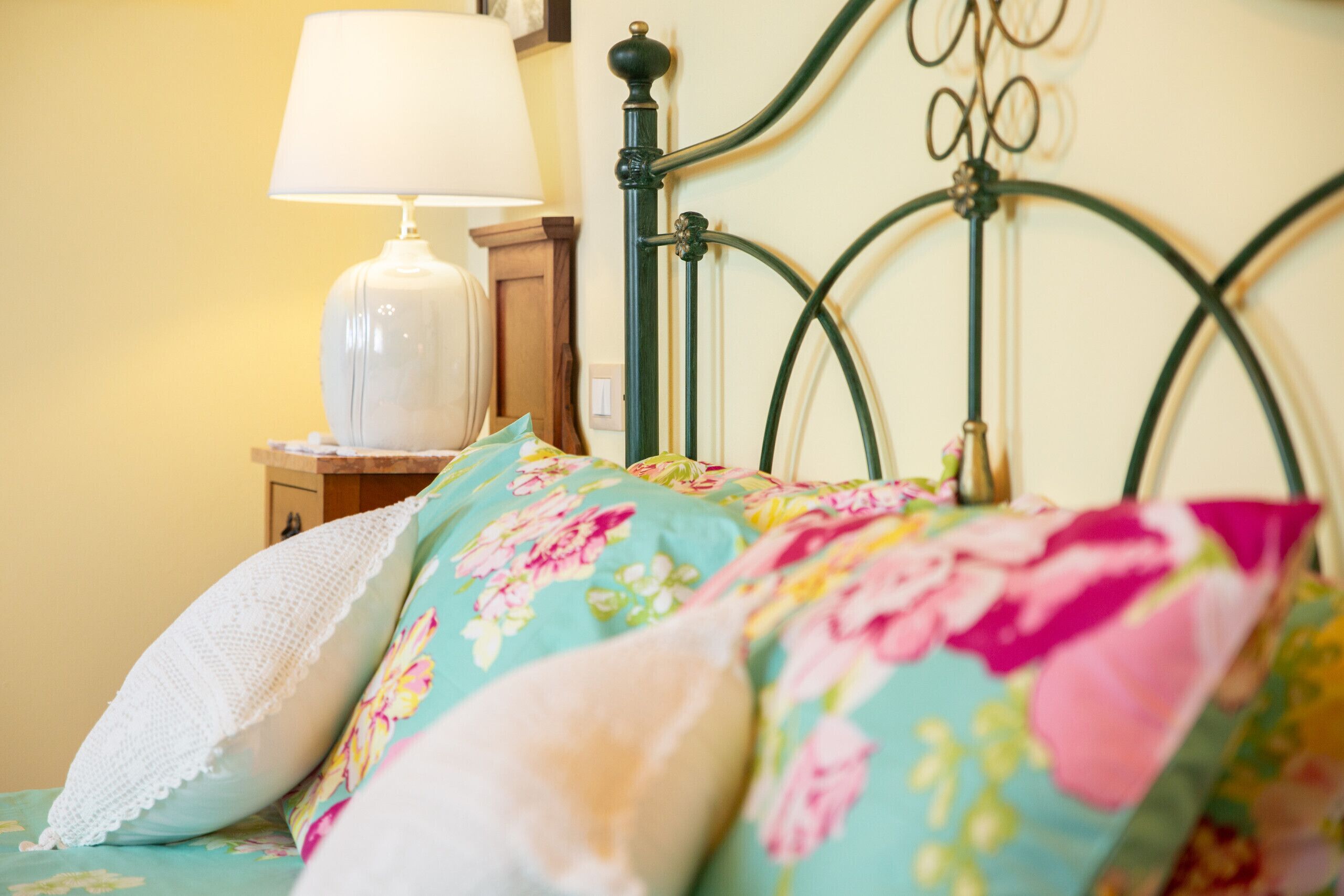 Un lit avec une literie à motifs floraux, un oreiller blanc et une table de chevet avec une lampe.