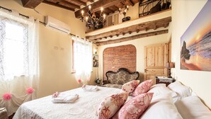 A bedroom with a large bed, a wooden ceiling, a brick fireplace, and a balcony with a view.