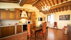 A kitchen with wooden cabinets, a dining table with chairs, a chandelier, and a window with curtains.