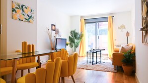 Ein modernes Wohnzimmer mit einem Glastisch, gelben Stühlen, einer Couch und einem großen Fenster mit Vorhängen.