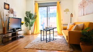 Ein Wohnzimmer mit einer Couch, einem Fernseher, einem Couchtisch und einer Pflanze.