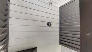 A white exterior wall with horizontal siding, a metal door with a handle, and a small window with horizontal blinds.
